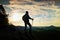 Silhouette of alone hiker with poles in hand. Tourist with sporty backpack stand on rocky view point above misty valley. Sunny spr