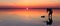 Silhouette of alone man takes a picture of a vibrant sunset reflected in shallow waters of solt lake. Banner size