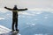 Silhouette of alone tourist standing on snowy mountain top in winner pose with raised hands enjoying view and achievement on