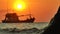 Silhouette of the anchored fishing boat in the rays of the setting sun swinging in the waves