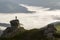 Silhouette of athletic climber tourist on high rocky formation on mountain valley filled with white puffy clouds and fog and