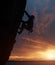 Silhouette of athletic person in safety harness. Climber on rope rock climbing on challenging cliff over water at sunset