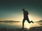 Silhouette of athletic runner jogging on the beach against sunrise.