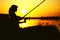 Silhouette of awoman with a fishing rod on the river bank