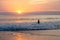 Silhouette back view of young woman entering into the Pacific Ocean during a fabulous pink sunset