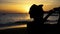 Silhouette back of young male travel backpacker with hat taking photos of summer beach scenery against sunset - travel