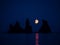 Silhouette of basalt rock formations Troll Toes on Black beach at noght with moon between the rocks. Reynisdrangar, Vik, Iceland