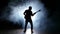 Silhouette bass guitarist man in smoke. Slow motion. Black background