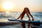 Silhouette of beautiful girl practicing yoga on surfboard at sunrise.