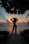 Silhouette of a beautiful slender girl on a sunset background and sun loungers on the ocean shore. Woman watch skyline
