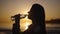 Silhouette of a beautiful woman on the background of the setting sun. A young woman drinks water from a bottle.