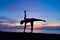 Silhouette of beautiful woman practicing yoga asana on the beach with sunrise on twilight blue vibrant sky