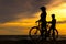 Silhouette biker lovely family at sunset over the ocean. Mom and daughter bicycling at the beach.