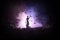 Silhouette of blurred giant lady justice statue with sword and scale standing behind crowd at night with foggy fire background.