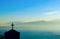 Silhouette of building with cross on top in front of mountain range blurred by deep fog across the channel