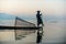 Silhouette Burmese fisherman wearing a hat standing at the back of a boat rowing with legs in the morning