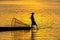 Silhouette of a Burmese man wearing a hat, using paddle legs to catch fish in the evening