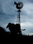 silhouette of a camel next to a windmill on a cloudy day