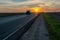 The silhouette of a car on the road against the background of the sun. The car is driving on the highway during sunset. The