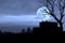 A silhouette of a cargo container lying outdoors with a flock of crows on a full moon