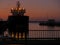 Silhouette of a cargo ship at port at sunset of sunrise. Orange purple tones. Vessel lights reflection in the water