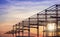 Silhouette of castellated beam metal structure of large industrial building in construction site against sunset sky