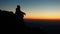 Silhouette of a Caucasian hiker sitting on a mountain edge, admiring the sunset