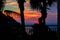 Silhouette child at sunset. Little boy stands on balcony amid red sea sunset and palm. Dramatic evening sunset over tropical sea.