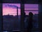 A silhouette of a child Toddler at the window looks at the pink dawn and sees smoke and urban houses