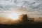 Silhouette of combine harvester from the back, hidden in the cloud of dust harvesting the crop of oilseed rape
