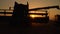 Silhouette of combine harvester pours out wheat into the truck at sunset. Harvesting grain field, crop season.