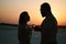 Silhouette of a couple with glasses on sunset background, man and woman clanging wine glasses with champagne at sunset dramatic sk