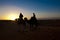 Silhouette of couple riding on camels at sunset in Sahara, Morocco. Woman and man riding on dromedaries at dawn.