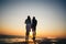 Silhouette of couple standing at the pier, watching the sunrise at the beach summer time