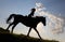 Silhouette of cowgirl riding horse through the dusk prairie