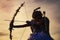 Silhouette of a cupid. Side view of teen girl archer against sunset. Little Cupid girl aiming at someone with an arrow
