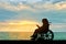 Silhouette of a disabled child girl sitting in a wheelchair reading a book on a sea sunset background