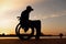 silhouette of a disabled person in a wheelchair on the background of the sunset