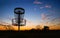 Silhouette of disc golf basket against sunset