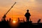 Silhouette of Engineer with blueprint and foreman worker team at construction site with blurred sunset sky background