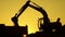 Silhouette of an excavator that loads sand into a truck at sunset. Concept construction and heavy industry, machine will