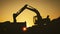 Silhouette of an excavator that loads sand into a truck at sunset. Concept construction and heavy industry, machine will