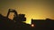 Silhouette of an excavator that loads sand into a truck at sunset. Concept construction and heavy industry, machine will