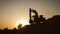 Silhouette of an excavator that loads sand into a truck at sunset. Concept construction and heavy industry, machine will