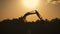 Silhouette of an excavator that loads sand into a truck at sunset. Concept construction and heavy industry, machine will