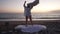 Silhouette of excited carefree young woman jumping on bed in twilight on sandy ocean beach outdoors. Wide shot of happy