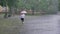 Silhouette of fat ginger girl is running in park under rain, holding umbrella, back view