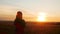 Silhouette of female figure standing in a wheat field alone, young woman enjoying sunset,