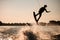 silhouette of female rider holding rope and skillfully jumping on wakeboard over splashing water.