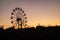 Silhouette of a ferris wheel at sunrise sunset of the sun on a background of trees and grass